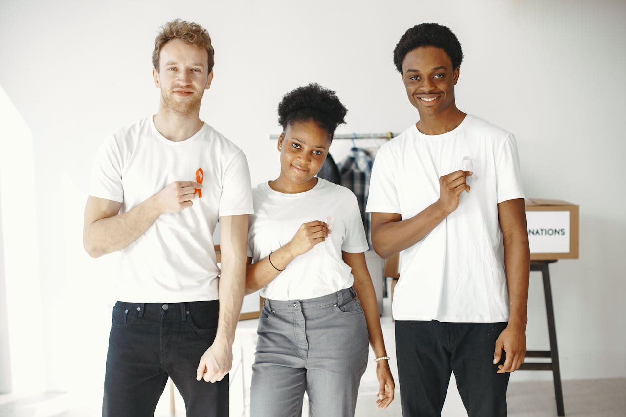 A diverse group of three smiling volunteers in white shirts displaying ribbons, promoting unity and awareness.